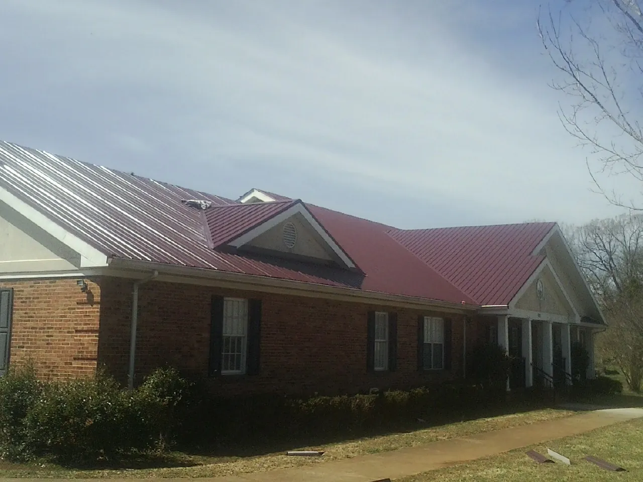 Red metal roof with gabled entries on a long brick building, from a Hail Damage Roof Repair job in Stilwell