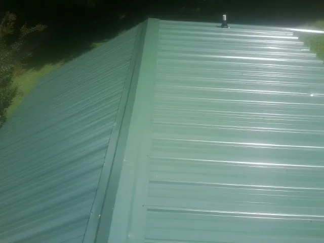 New green metal panels meeting at the ridge of a roof — Flat Roof Repair work by our crew in Stilwell