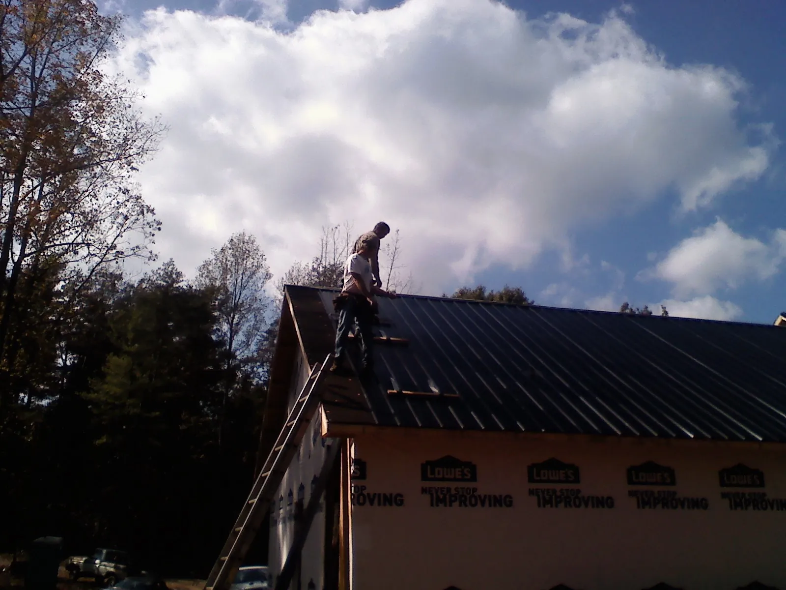 Roofer fastening dark metal panels high against a cloudy sky, from a Roof Inspection job in Stilwell
