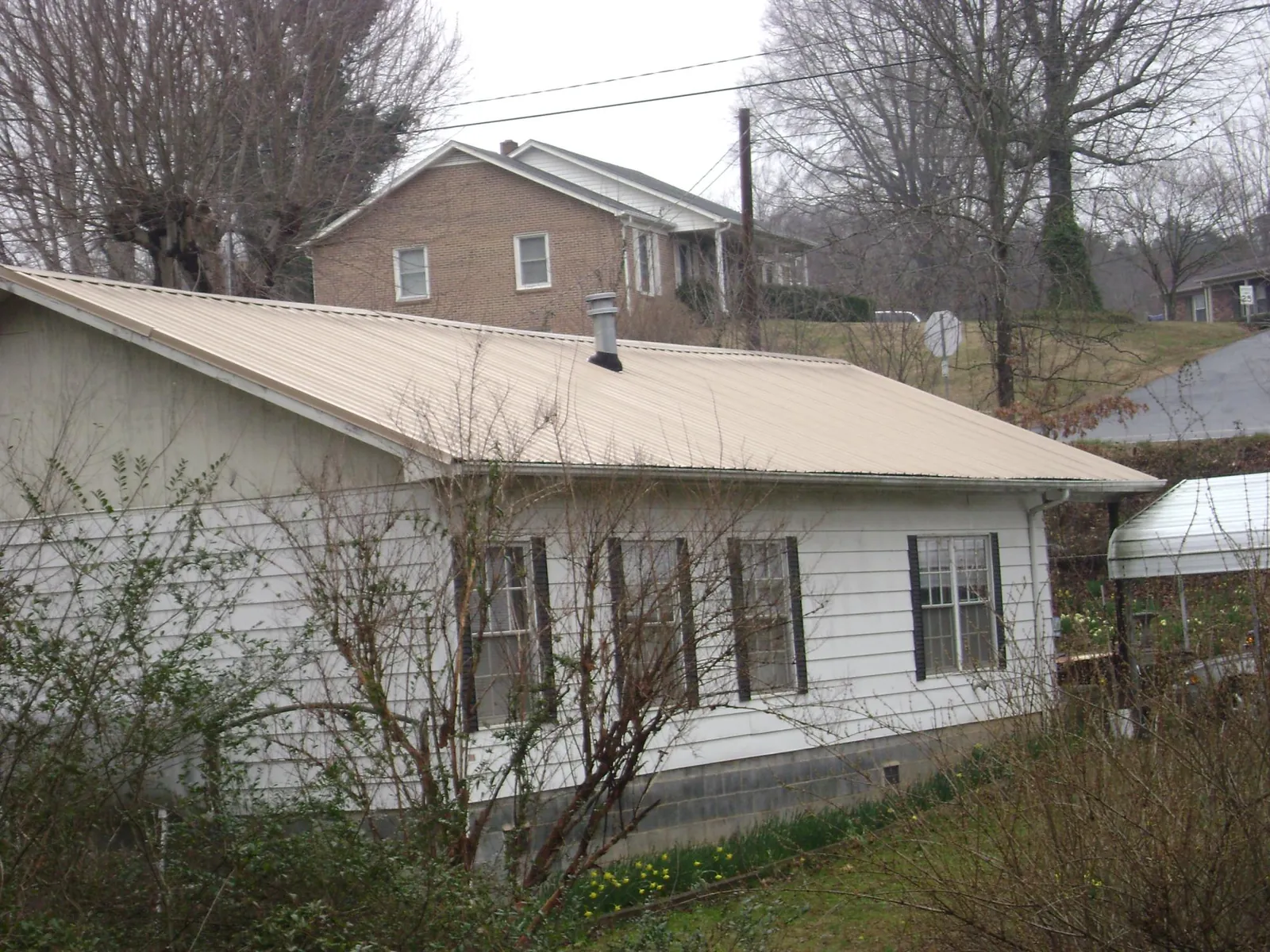 Tan metal roof on a white sided house set into a hillside — Commercial Roofing by Roofing Brothers in Stilwell