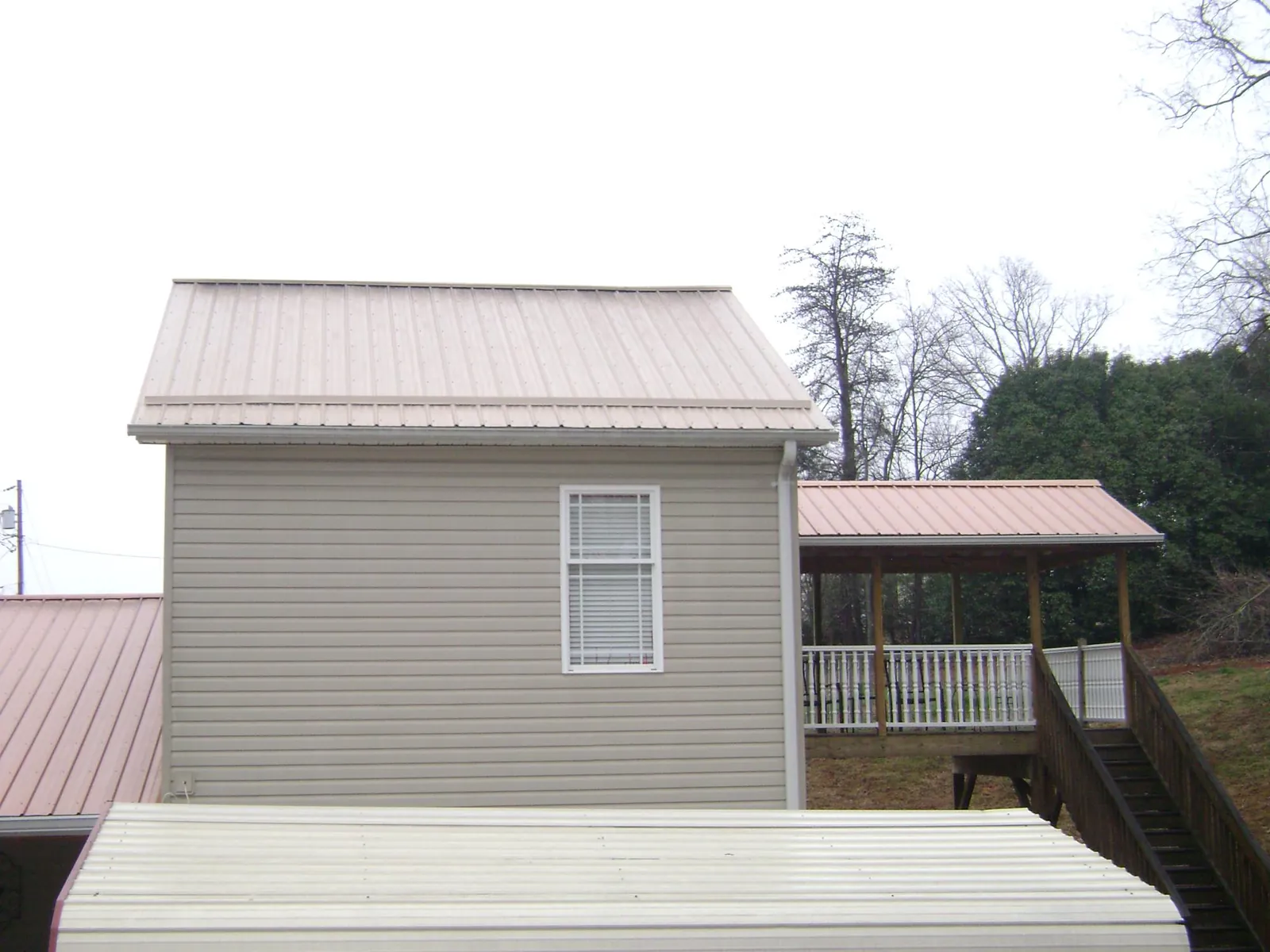 Tan metal roofs on a two story addition and attached porch, from a Roof Replacement job in Stilwell